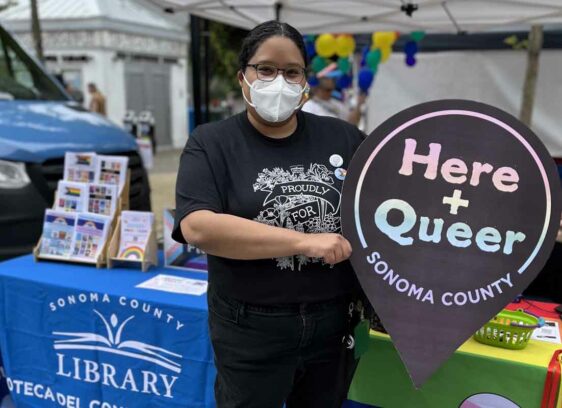Photo courtesy of Sonoma County Library PRIDE Librarian Zayda Delgado poses at Sonoma County Pride 2022 with the ‘Here + Queer’ logo. Delgado is the lead librarian designing the archival project.