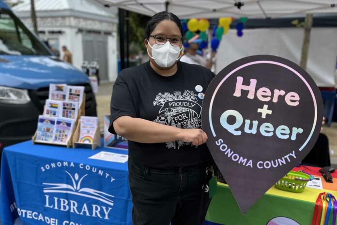 Photo courtesy of Sonoma County Library PRIDE Librarian Zayda Delgado poses at Sonoma County Pride 2022 with the ‘Here + Queer’ logo. Delgado is the lead librarian designing the archival project.