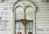 Two musicians standing with an acoustic guitar in front of a weathered white building