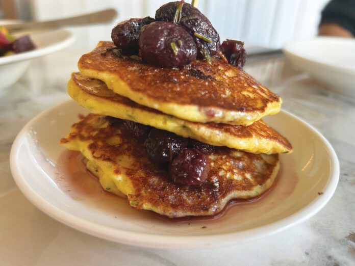 A stack of pancakes topped with roasted grapes and served on a plate.