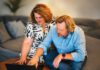A woman and man sit together on a couch, looking at a laptop