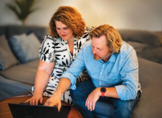 A woman and man sit together on a couch, looking at a laptop