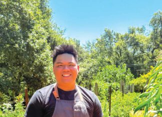 A man wearing an apron stands in a garden