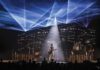 Third Eye Blind, a five-member rock band, performs onstage beneath blue laser lights and a central white spotlight as an audience watches.