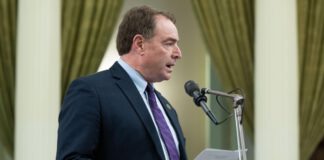 Assemblymember Damon Connolly speaks into a microphone while holding papers at a podium in the California State Capitol.