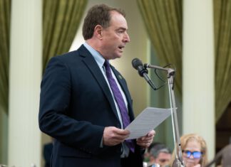 Assemblymember Damon Connolly speaks into a microphone while holding papers at a podium in the California State Capitol.