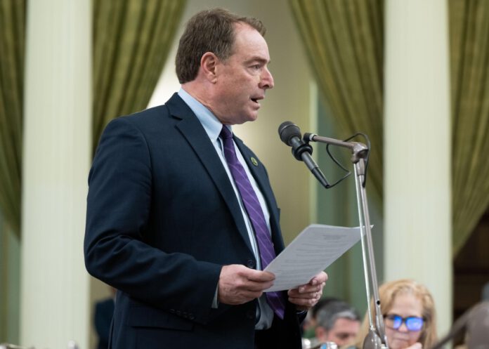 Assemblymember Damon Connolly speaks into a microphone while holding papers at a podium in the California State Capitol.