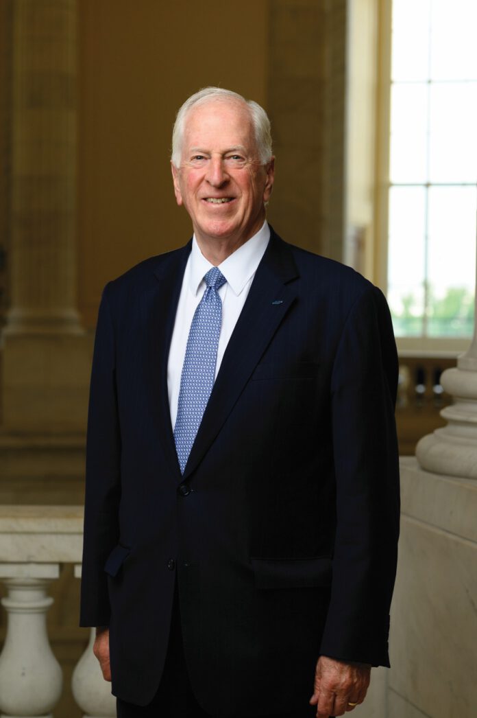 Rep. Mike Thompson stands smiling in a dark suit, white shirt and blue tie inside a government building.