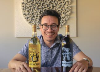 A smiling man in glasses holds two wine bottles labeled "Meowsling" and "Pinotmeow," each featuring a cartoon cat.