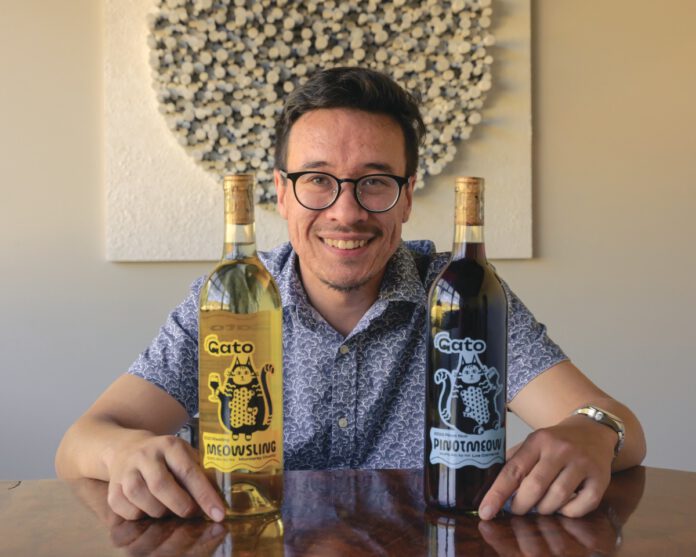 A smiling man in glasses holds two wine bottles labeled 