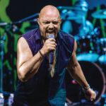 Mindcrimes: Queensryche’s Geoff Tate A bald singer in a sleeveless purple shirt sings into a microphone on a blue-lit stage with drums behind him.