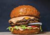A double cheeseburger with melted cheese, pink sauce, lettuce, tomato, pickles and onion on a sesame bun.