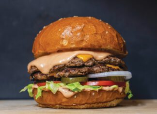A double cheeseburger with melted cheese, pink sauce, lettuce, tomato, pickles and onion on a sesame bun.