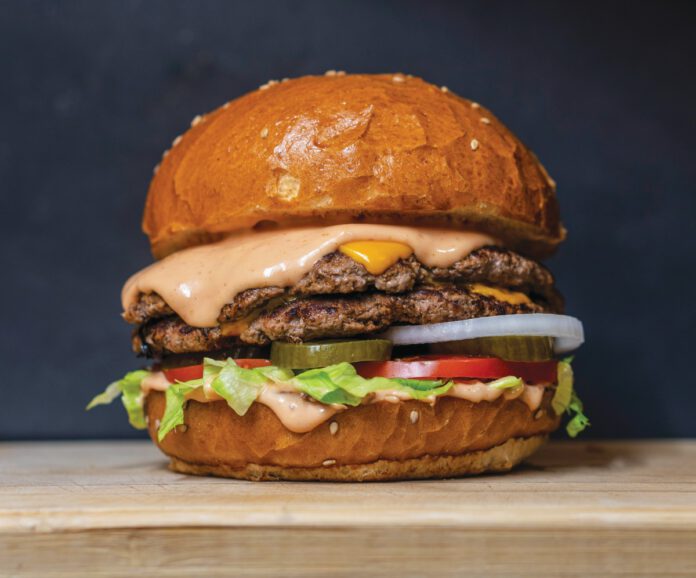 A double cheeseburger with melted cheese, pink sauce, lettuce, tomato, pickles and onion on a sesame bun.